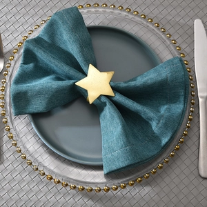 Matte gold star napkin ring on blue cloth with elegant table setting and gray placemat