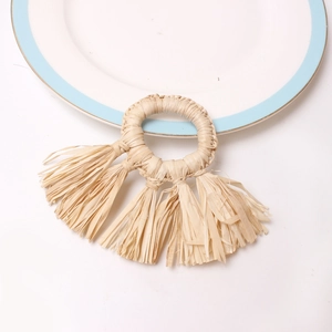 Handgemaakte raffia servetring met drie kwastjes op een wit keramisch bord