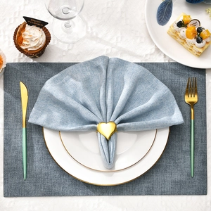Golden heart-shaped napkin ring with blue fabric napkin on a grey placemat setting