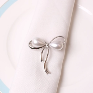 Detailed view of silver bow napkin ring with pearls on a white ceramic plate