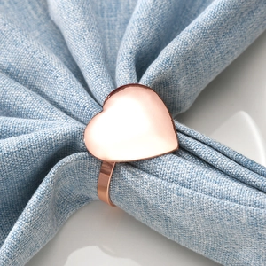 Elegant rose gold heart napkin ring displayed on a blue fabric napkin over white plate