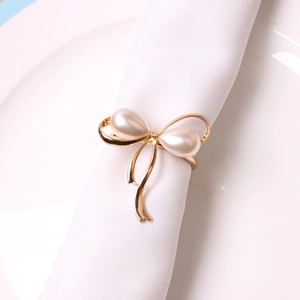 Golden bow napkin ring with white pearls on a white napkin for elegant table settings
