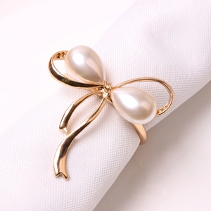 Golden bow napkin ring with large water-drop pearls on a white linen napkin
