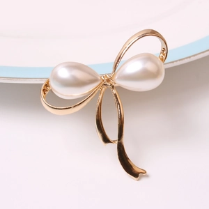 Elegant gold bow napkin ring featuring large white pearls on a decorative ceramic plate