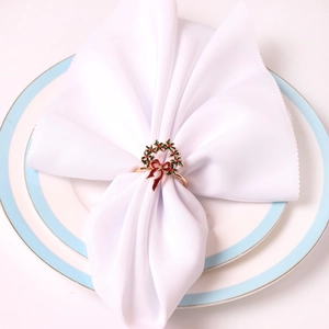 Détail d'un rond de serviette de Noël avec couronne verte et nœud rouge sur assiette
