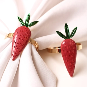 Detail of red carrot napkin rings with green leaves and gold metal holders for table decor