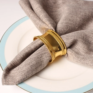 Golden oval napkin ring with beaded edges on a blue plate with a linen napkin