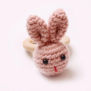 Macro detail of hand-knitted pink rabbit head with ears on a natural wooden ring