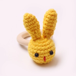 Close-up of handmade yellow crochet bunny rattle with smooth natural wood teething ring