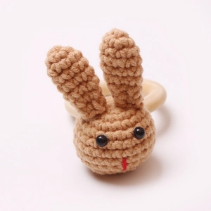 Macro detail of hand-crocheted khaki rabbit baby rattle with natural wooden teething ring