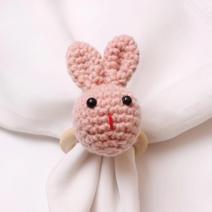 Close-up of pink hand-knitted bunny napkin ring on white fabric with a natural wooden loop