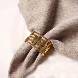 Golden hollow geometric napkin ring with elegant mirror finish on a grey napkin