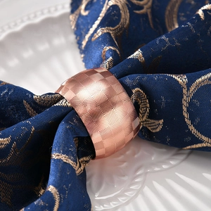 Rose gold drum-shaped metal napkin ring with geometric texture on elegant table setting