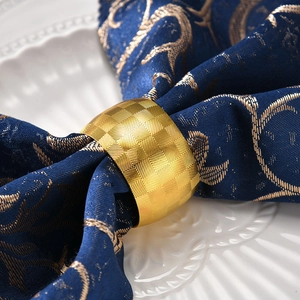 Elegant gold drum-shaped metal napkin ring with geometric texture on dark blue napkin