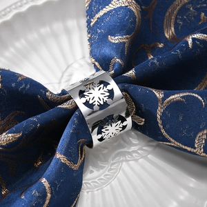 Silver metal snowflake napkin ring with intricate hollow design on navy blue fabric