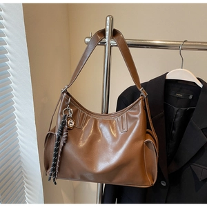 Detail der karamellbraunen Hobo-Tasche mit breitem Gurt und gewebtem Quasten-Anhänger
