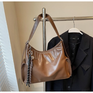 Detail einer braunen Leder-Tote-Bag mit weißen Kontrastnähten und dekorativem Webanhänger