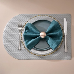 Top view of a rose gold spherical napkin ring on a dark teal cloth with silver placemat
