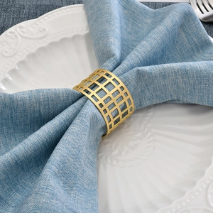 Golden geometric hollow mesh napkin ring on blue linen napkin over luxury white china plate