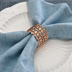 Macro detail of rose gold wavy镂空 napkin ring on a textured blue linen cloth