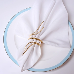 Artistic gold metal napkin ring with hammered texture in a spiral wave design on white napkin