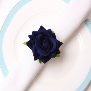 Close-up of a handmade dark blue rose napkin ring with green leaves on a ceramic plate