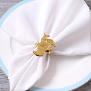 Detail eines goldenen Serviettenrings in Geisterform auf weißem Tuch und Keramikteller