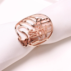 Détail d'un rond de serviette or rose avec calligraphie arabe évidée sur tissu blanc