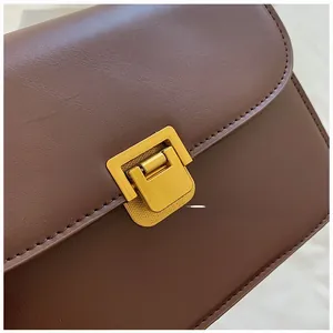 Close-up of elegant gold square buckle on dark brown leather flap bag with matte finish