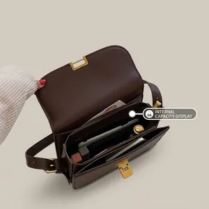 Detail of dark brown leather crossbody bag with gold buckle and multiple compartments