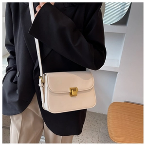 Detail of a creamy white crossbody bag featuring a vintage gold-tone twist lock and slim strap