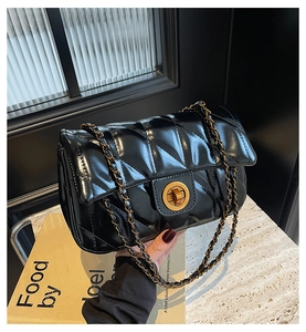 Détail de la texture en cuir noir matelassé avec fermoir rotatif doré sur le sac bandoulière