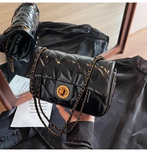 Détail d'un sac noir en cuir ciré matelassé avec fermoir doré et bandoulière chaîne