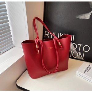 Détail du sac cabas de mariée rouge avec logo doré sur un bureau blanc stylé