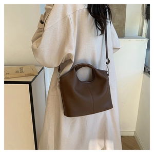 Brown litchi leather bucket bag worn with a white trench coat in a modern setting
