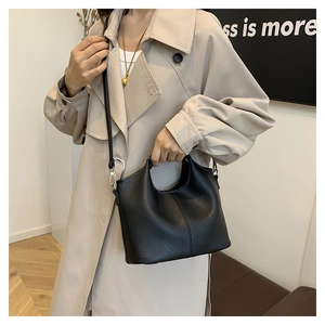 Detail of black lychee texture handbag with round cutout handle worn with a trench coat