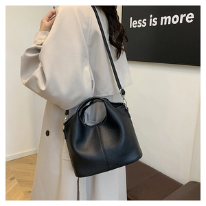Detail of black lychee grain leather bucket bag with silver hardware on beige trench coat