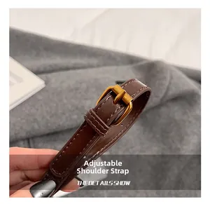 Detail view of adjustable brown leather shoulder strap with gold buckle and white stitching