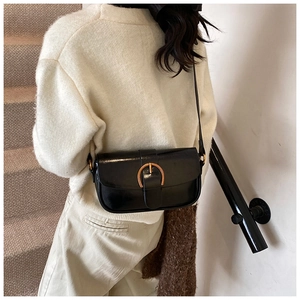 Detail of a black leather shoulder bag with a gold buckle worn by a model on stairs