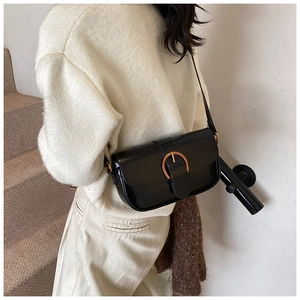 Close-up of black leather shoulder bag with gold horseshoe buckle on a knit sweater
