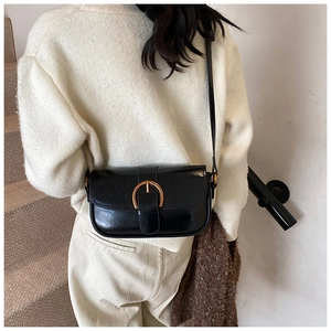 Detail of black glossy leather crossbody bag with elegant gold horseshoe buckle hardware