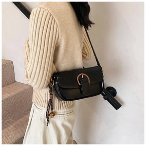 Detail of black glossy shoulder bag featuring golden horseshoe buckle and silk scarf charm