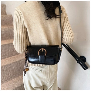 Detail of a vintage black leather crossbody bag with a gold buckle and bell charm