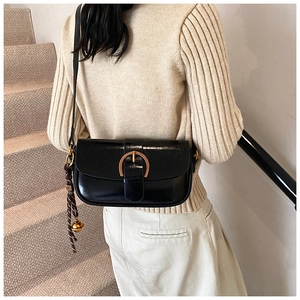 Detail of glossy black leather bag featuring a large gold horseshoe buckle and silk tassel