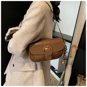 Detail of dark brown leather crossbody bag with gold bell and woven rope on tweed blazer
