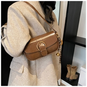 Close-up of brown leather underarm bag with gold D-ring buckle and decorative charm