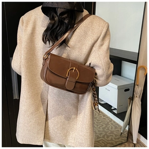 Close-up of brown glossy shoulder bag with golden D-ring buckle on tweed jacket