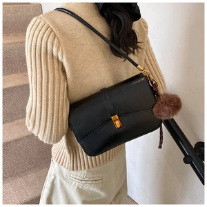 Detail of minimalist black matte shoulder bag with gold metal buckle and plush pompom charm