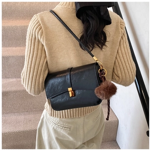 Detail of black leather crossbody bag featuring gold square lock and brown fur ball charm