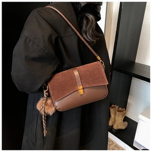 Detail of a brown suede crossbody bag with gold buckle and plush charm on a black coat